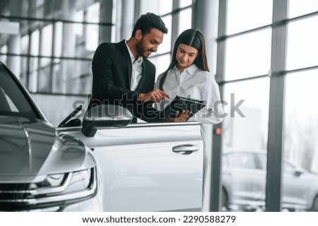 Man in formal clothes is consulting woman about the automobile in the car dealership.
