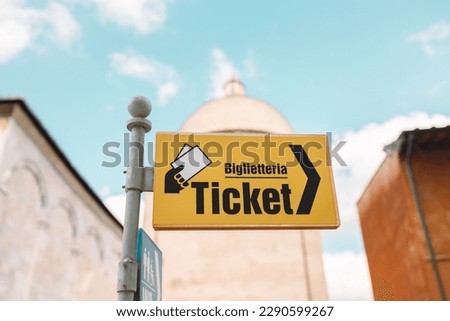 Yellow sign pointer and arrow directing to tickets in the streets of Pisa, Italy. Cloudy blue skies above. High quality photo