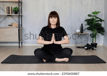 yoga and meditation concept - young woman doing yoga sitting on yoga mat in living room at home