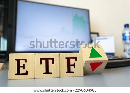 Wooden cubes with the inscription ETF and a cube symbolizing the rise and fall of financial markets.