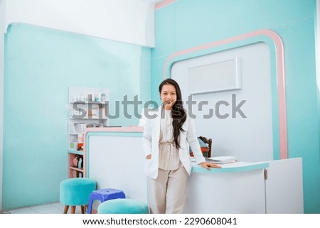 Female vet standing with the reseptionist desk on the background. smiling and put one of her hand on the desk and the another one inside her pocket