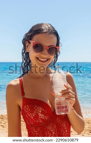 Young woman in a red bathing suit on the beach holding a bottle of water.