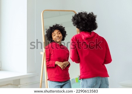 Love yourself. Beautiful young smiling african american woman dancing enjoying her mirror reflection. Black lady looking at mirror looking confident and happy. Self love concept Royalty-Free Stock Photo #2290613583