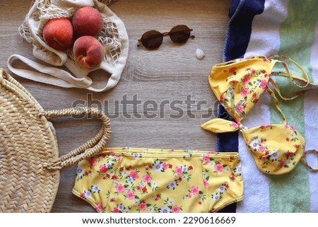 Floral bikini, striped beach towel, sunglasses, straw bag, seashell and tote with peaches on wooden background. Top view.