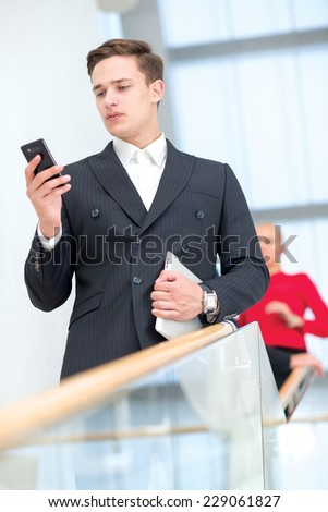 Young successful businessman confidently checks his mobile phone, looking for solution of his business issue.