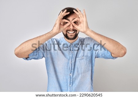 Portrait of young man making glasses mask with fingers, fooling around isolated on white background