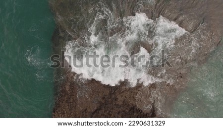A picturesque view of rocks and stormy waves on the shore of a large island. Air shot