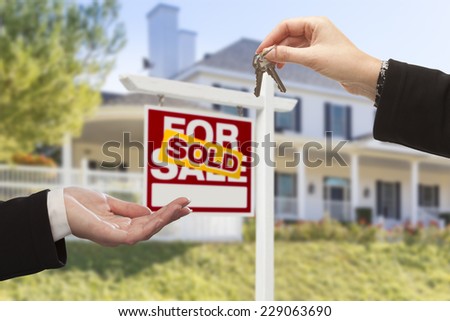 Agent Handing Over Keys to a New Home with Sold Real Estate Sign and House in the Background.