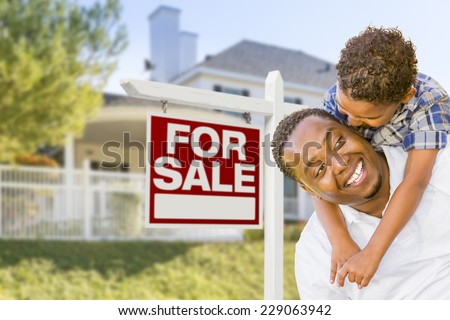 African American Father and Mixed Race Son In Front of Home For Sale Real Estate Sign and New House.