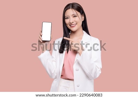 Beautiful Asian business woman holding smartphone mockup with blank screen isolated on pink background.