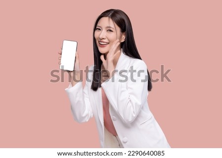 Beautiful Asian business woman holding smartphone mockup with blank screen isolated on pink background.