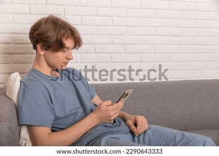 Enjoying Weekend. Teenage boy using smart phone sitting on sofa at home Royalty-Free Stock Photo #2290643333