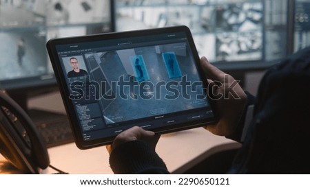 Male security officer controls CCTV cameras in office, uses digital tablet and computers with surveillance camera footage playback on screens. High tech security system. Monitoring and social safety. Royalty-Free Stock Photo #2290650121