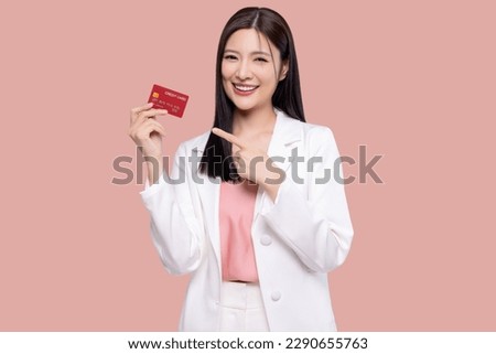 Beautiful young Asian business woman wearing white suit smiling, showing, presenting credit card for online payment isolated on pink background.