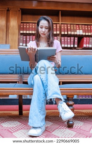 College student sitting on a bench in the library and reading a book (vertical photo)