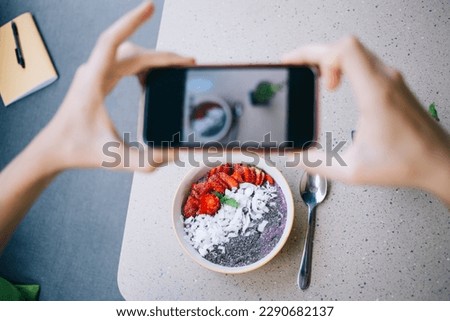 Cropped view of blurred unrecognizable female user making content photos for food blog during leisure time in cafe interior with organic food, selective focus on fruit bowl foe eating on breakfast