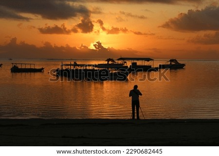 Silhouette of photographer take picture of a stunning sunset in Tanjung Benoa Beach Bali. Calm sea, silhouette of a fishing boat, Nature Background.