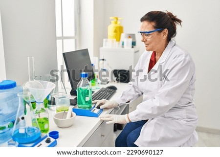 Middle age hispanic woman wearing scientist measuring liquid at laboratory