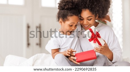 happy mother's day. african american baby daughter giving  gift box to her mom for holiday in bed at home  
