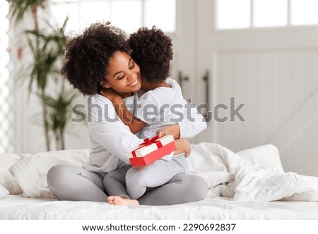 happy mother's day. african american baby daughter giving  gift box to her mom for holiday in bed at home  
