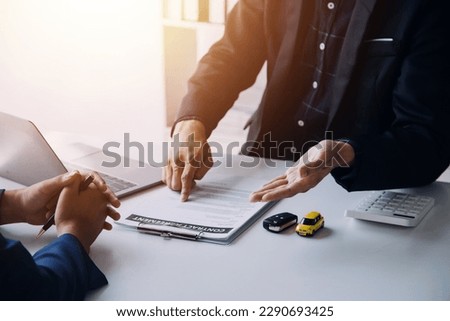 Closeup of Asian female signing car insurance document or lease paper contract or agreement. Buying or selling new or used vehicle with car keys on table.