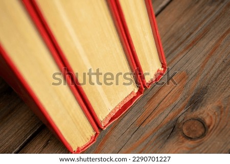 The spines of books with a red cover. Three books stand side by side on a wooden table. The end of the book is dense sheets of a closed book.