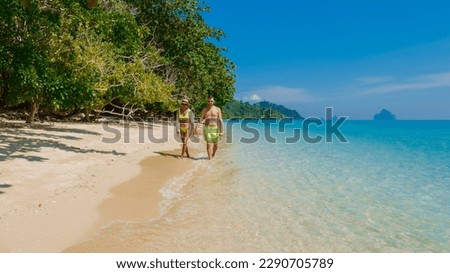 the backside of a couple of men and women sitting at the beach of Koh Kradan island in Thailand during vacation on a sunny day at holiday on the beach