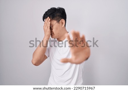 Young asian man standing over white background covering eyes with hands and doing stop gesture with sad and fear expression. embarrassed and negative concept.  Royalty-Free Stock Photo #2290715967