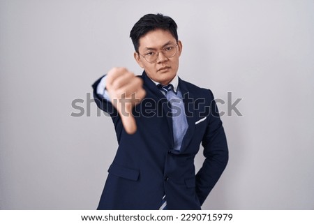 Young asian man wearing business suit and tie looking unhappy and angry showing rejection and negative with thumbs down gesture. bad expression. 