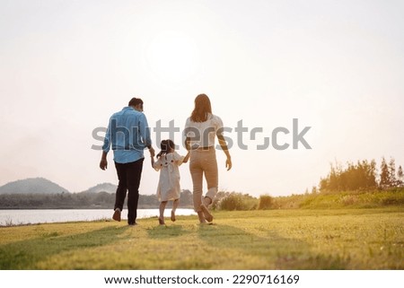 Happy family in the park sunset light. family on weekend running together in the meadow with river Parents hold the child hands.health life insurance plan concept. Royalty-Free Stock Photo #2290716169