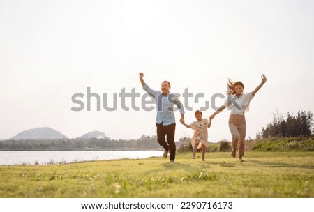 Happy family in the park sunset light. family on weekend running together in the meadow with river Parents hold the child hands.health life insurance plan concept. Royalty-Free Stock Photo #2290716173