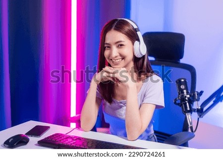 Professional gamer. Young asian pretty woman sitting on chair with computer pc in living room. Happy female Professional Streamer chinese wearing headphone playing game online in dark room neon light