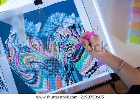 Little girl making diamond painting or pearl mosaic picture. Colorful small pearls stick on image on canvas. Photo series. Trending calming kids leisure activity.