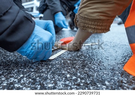 a policeman uses solvent to remove a glued climate activist from the asphalt Royalty-Free Stock Photo #2290739731