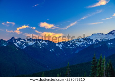 Alpenglow on clouds over a rugged mountain range, Mt. Rainier National Park, Washington, USA.