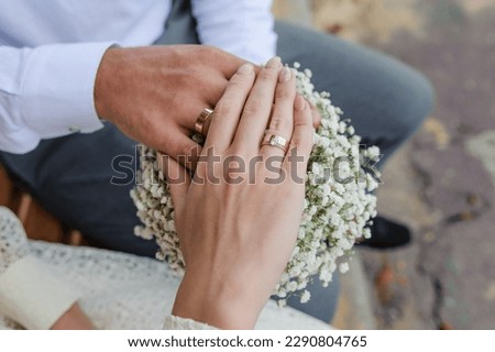 Wedding rings on the hands of the newlyweds, a bouquet of flowers in the background. Gold rings on the hand of a man and a woman Royalty-Free Stock Photo #2290804765