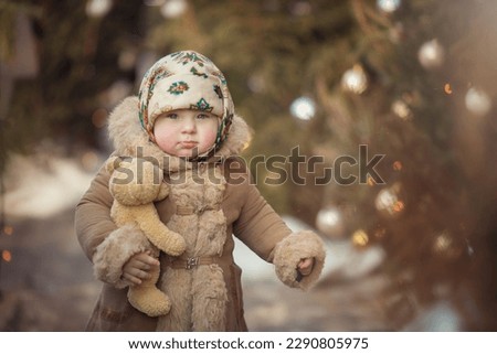 Little girl in winter clothes with a toy near the Christmas tree