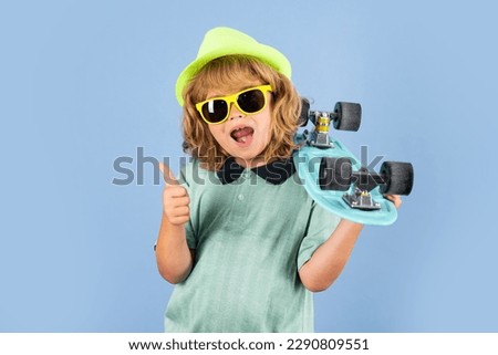 Excited child with thumb up. Funny happy kid in casual wear holding longboard looking happy and excited. Studio isolated portrait of kid with skateboard.