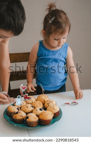 Two children daughter and son preparing muffins in home kitche, decorating freshly baked homemade cakes with christmas pictures. Delicious food.