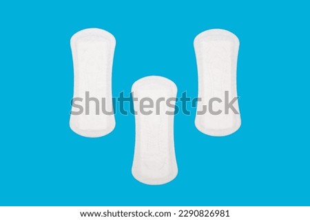 Three women's sanitary menstrual pads are located on a blue background. Feminine hygiene product in the form of sanitary napkins. Clean menstrual pads are ready to use. Women's panty liners