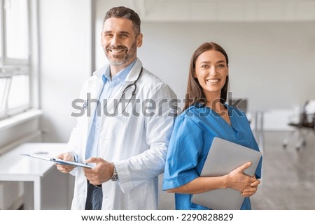 Team of two professional doctors working together in clinic, man posing with digital tablet, woman with clipboard, looking and smiling at camera. Healthcare and medicine concept