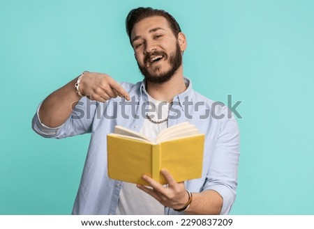 Happy lebanese man reading funny interesting fairytale story book, leisure hobby, knowledge wisdom, education, learning, study, wow. Handsome arabian guy isolated alone on blue studio wall background