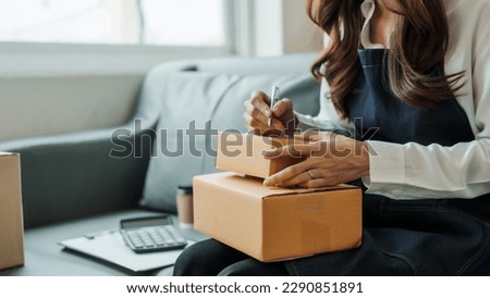 Writing clients address, Young pretty Asian female influencer small businesses SME owners female entrepreneurs working on receipt box and check online orders, sitting on sofa of home online business.