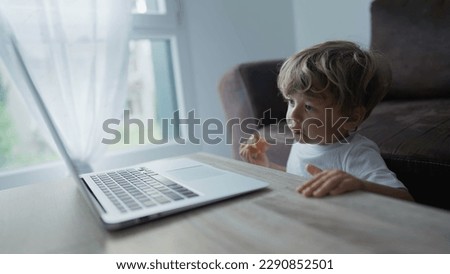 Child watching cartoons on laptop computer at home while eating apple fruit snack