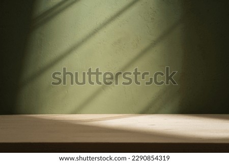 Empty table on dark green plaster wall background. Composition with window shadow on the wall and light reflections. Mock up for presentation, branding products, cosmetics food or jewelry.