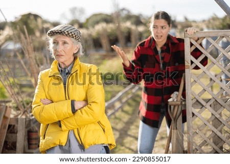 Two angry casual women neighbors of different ages arguing during the vegetable garden season on sunny day of spring Royalty-Free Stock Photo #2290855017