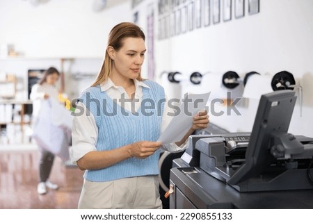 Female employee of the printing house adjusts the plotter using a computer
