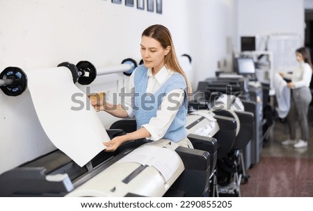 Woman working in publishing facility, loading large format paper in printer. Royalty-Free Stock Photo #2290855205