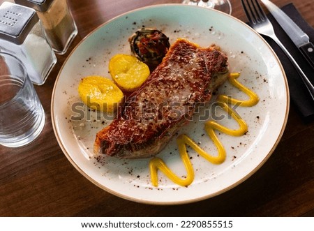 hot baked entrecote with vegetables decorated with onion rings is served in baking dish Royalty-Free Stock Photo #2290855515