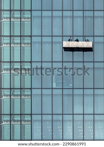 A glass building wall with window washers descending the facade on a lift platform in Tokyo, Japan Royalty-Free Stock Photo #2290861991